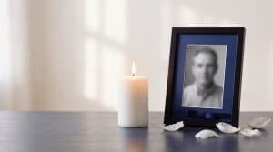 A lit memorial candle next to a framed photograph on a quiet table, marking the anniversary of a loved one's death