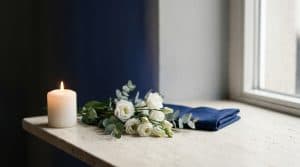 Quiet remembrance scene representing mourning, with a single candle and white flowers on a stone ledge in soft warm light